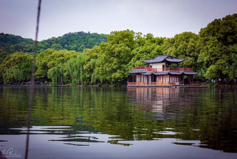 Traditional chinese house reflected on the water of the West Lake with green three in the background in a calm early-autumn afternoon