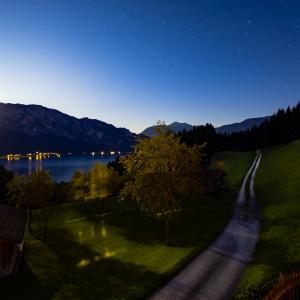 Long exposure photo of the moon rising in a blue sky at night. In the background alps and the Attersee, Austria