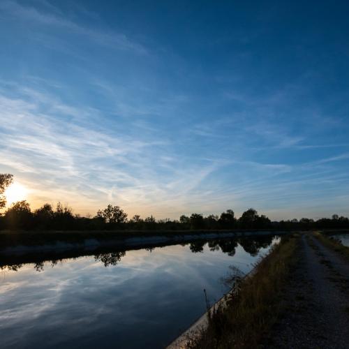Deep blue sky taken at sunset with some yellow light coming from the horizon. Clouds are reflected on the calm water of the river