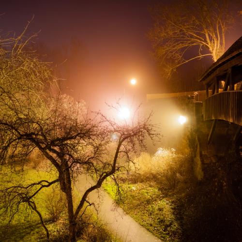 Long exposure of an old medieval bridge in Rothenburg ob der Tauber with a strong orange light illuminating a tree at night.