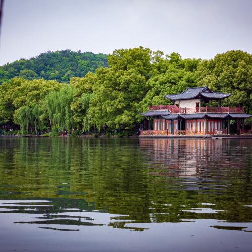 Traditional chinese house reflected on the water of the West Lake with green three in the background in a calm early-autumn afternoon